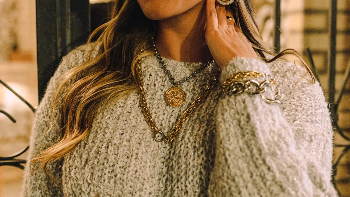 Boucles d’oreilles et colliers dorés portés avec un pull en maille