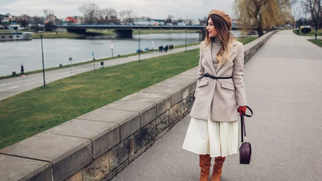 Femme portant une jupe longue fluide avec bottines et manteau clair, look chic d’automne.