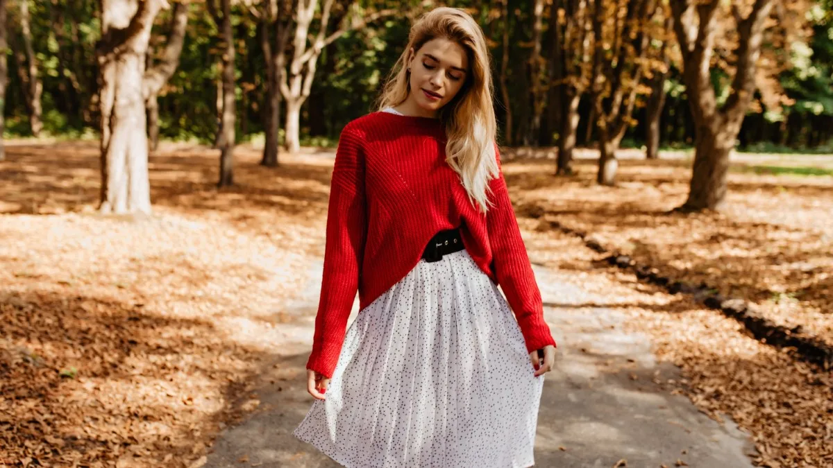 Jupe longue plissée couleur blanche, associée à un pull rouge et des bottines marron.