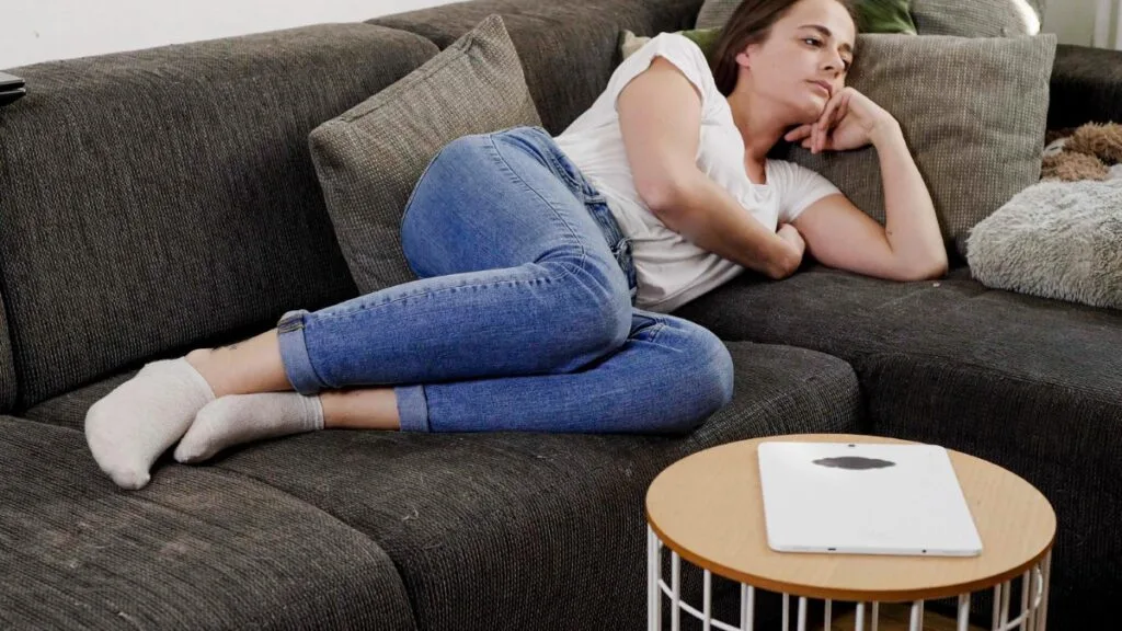 Femme allongée sur un canapé, pensive, qui culpabilise de ne rien faire mais essaie de se reposer