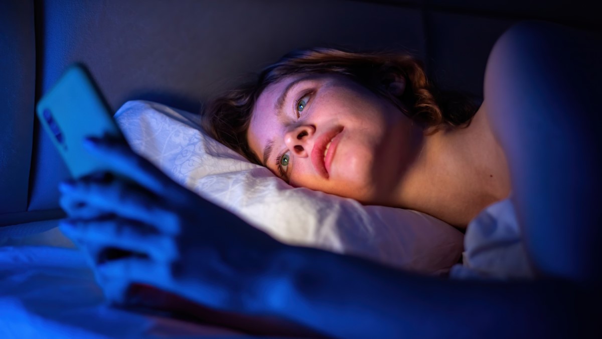 Personne dans son lit, téléphone allumé dans l’obscurité, évoquant l’insomnie liée à la lumière bleue.