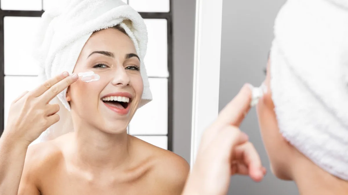 Une jeune felle appliquant une crème hydratante sur le visage avant un maquillage de fêtes