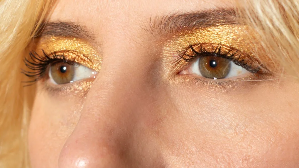 Gros plan sur un maquillage des yeux doré champagne avec mascara pour un look de fêtes