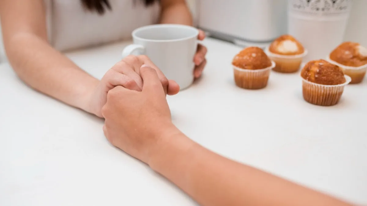 Deux mains qui se rejoignent autour d’une tasse, lumière douce rosée.