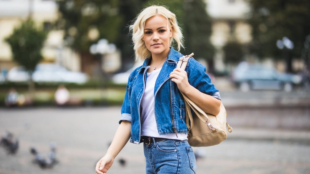 Jeune femme étudiante en jean, t-shirt, surchemise et veste légère sur un campus au printemps.