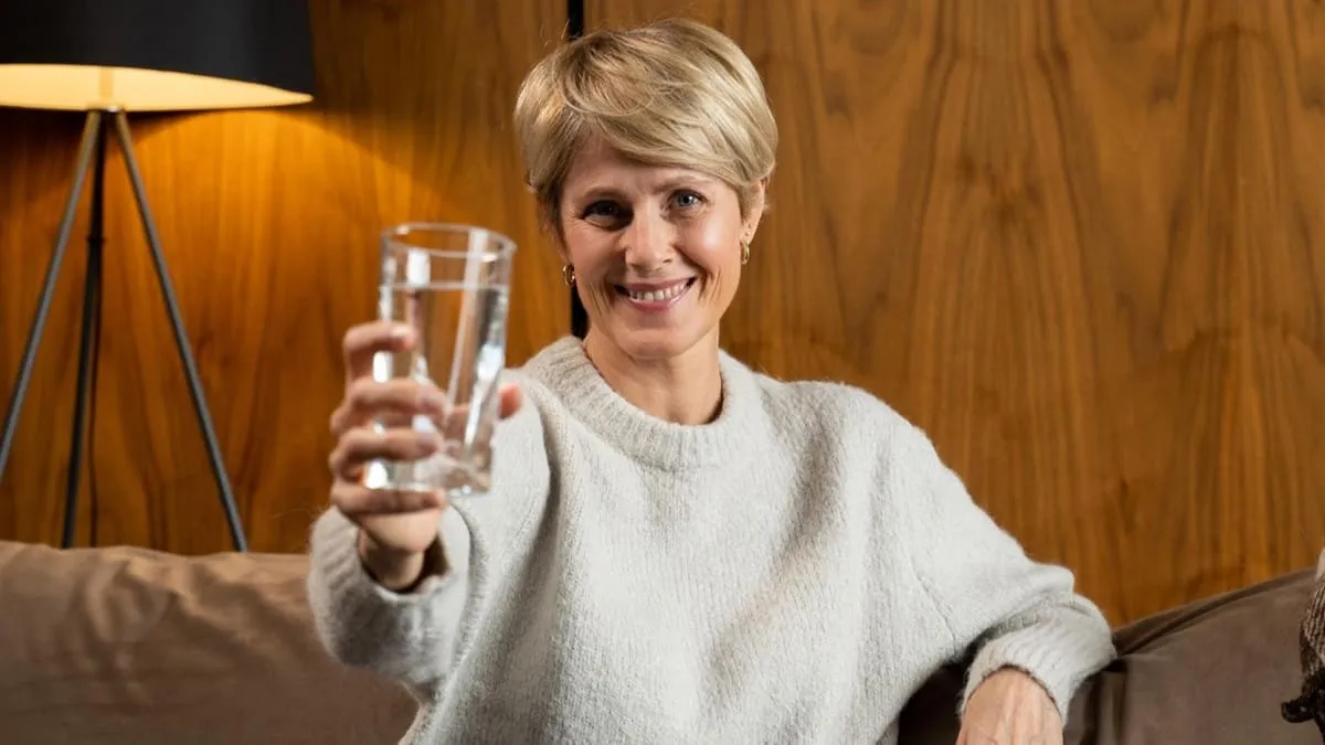 Une femme heureuse, malgré sa ménopause prend son complément alimentaire avec un verre d'eau.
